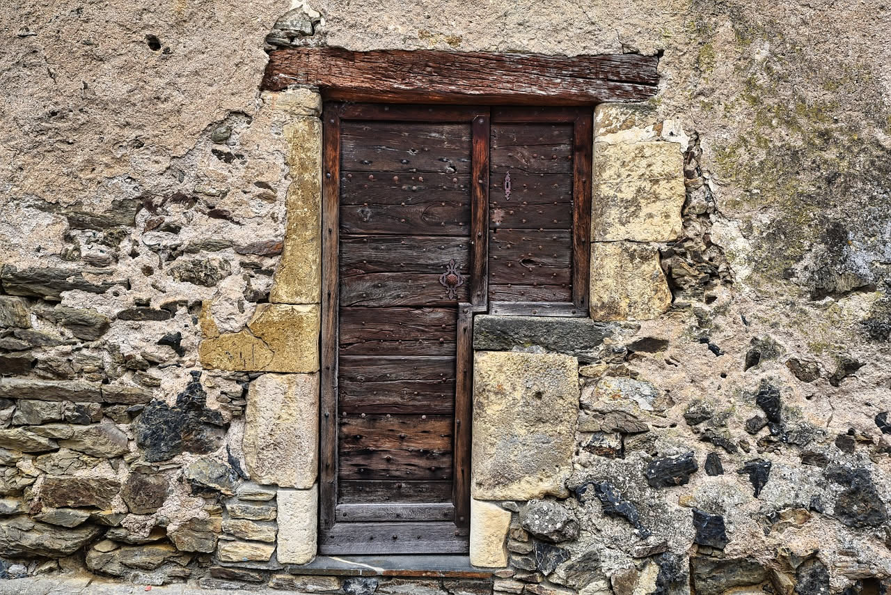 Cerniera in ottone di una porta bianca con segni di usura, mano che applica lubrificante dalla bottiglia trasparente