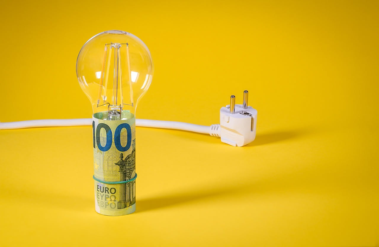 Tre lampadine LED di diverse dimensioni e colori di base (bianco freddo, bianco caldo, ambrato) poste su un tavolo di legno con uno sfondo di presa elettrica
