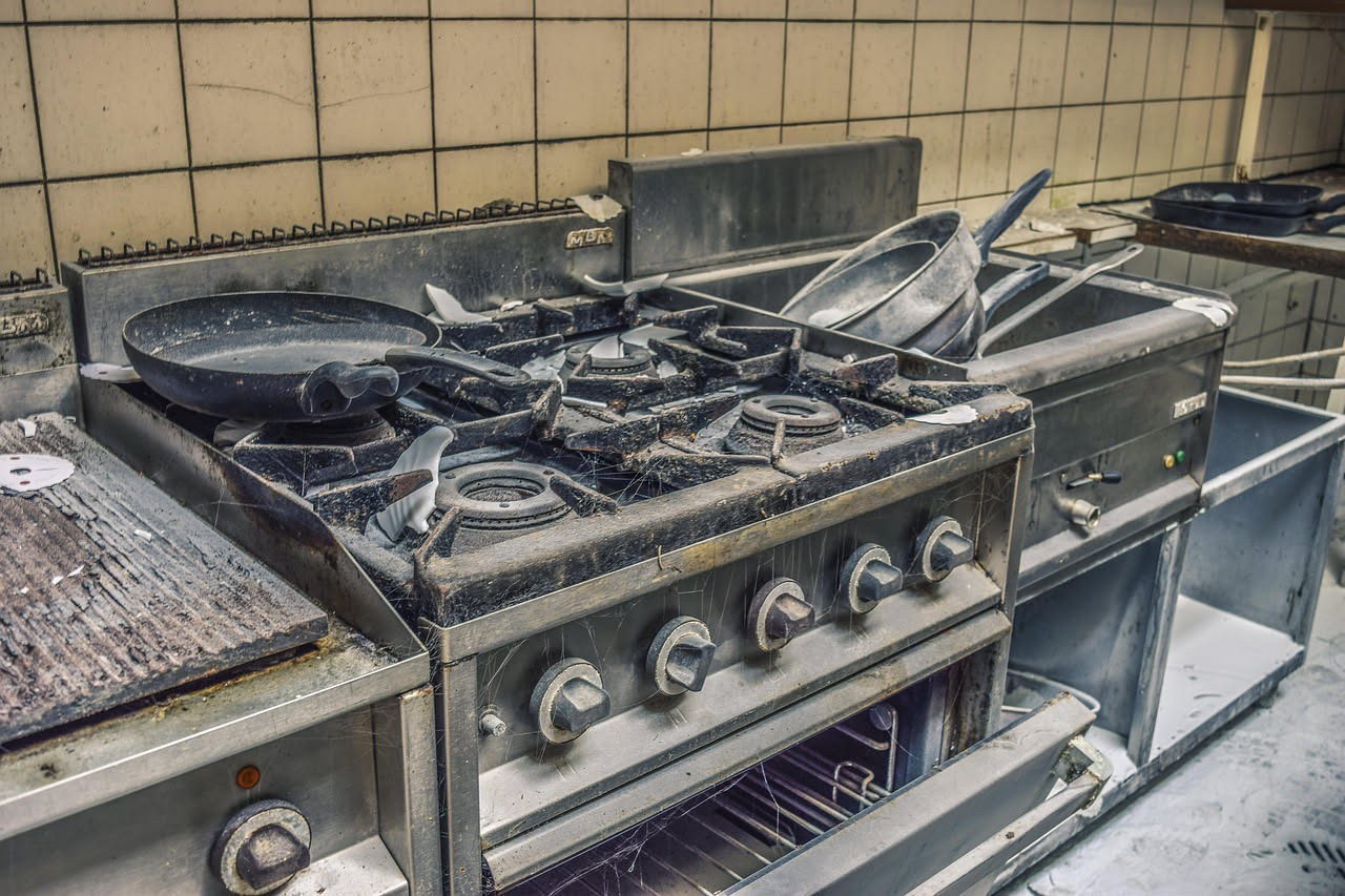 Interno di forno con accumuli di residui bruciati neri sulle pareti, porta aperta, ripiano con pane in cottura