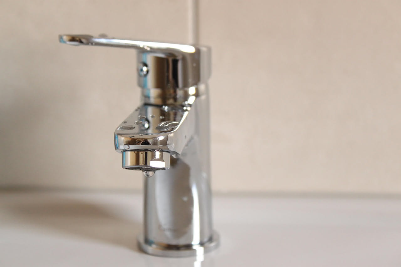 Mano che regola il dado sotto un lavandino con una chiave inglese, con gocce d'acqua visibili sul tubo di rame