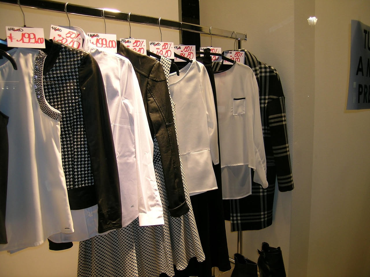 Cinque capi di abbigliamento appesi su una fila di ganci in legno: maglietta rossa, camicia bianca, cardigan azzurro, pantaloni neri, vestito floreale