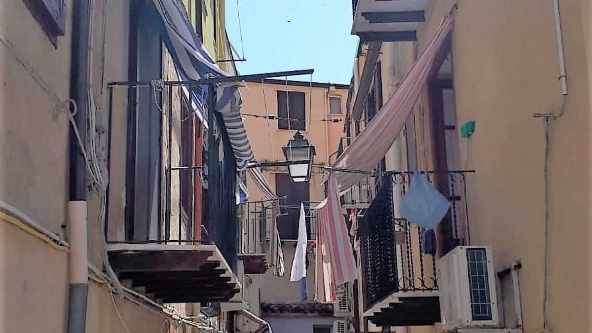 Bucato bianco e colorato steso su una corda tesa tra due pali su un balcone, con sole che filtra tra i vestiti e la città in background sfocata