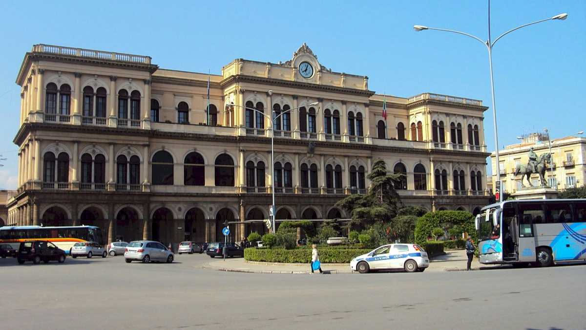 Portone in legno scuro di un palazzo storico italiano con numero civico in ottone, custoderia vuota, scale interne con pareti grigie, nessuna persona visibile