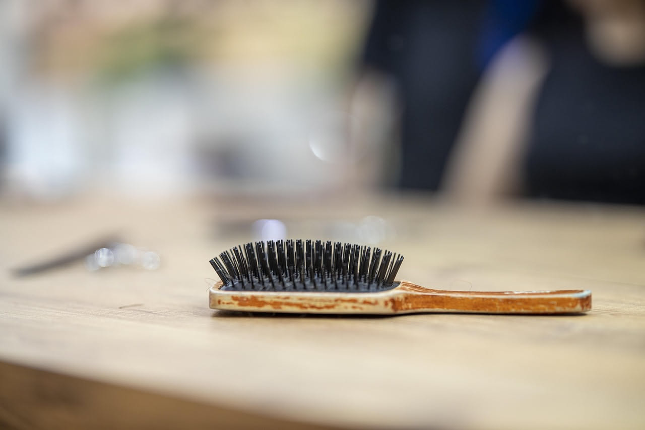 Spazzola per capelli bagnata sotto getto d'acqua calda con residui di capelli e schiuma di sapone, su sfondo bianco