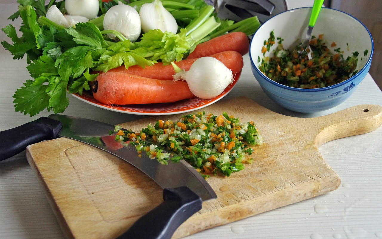 Sacchetto trasparente nel freezer pieno di scarti di verdura colorati: bucce di cipolla, gambi di prezzemolo, foglie di sedano, carota tagliata