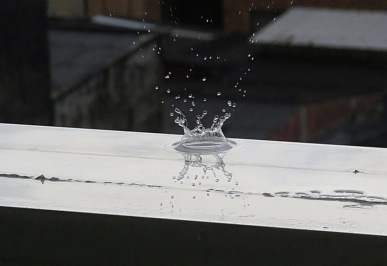 Balcone con sistema di raccolta acqua piovana: tubo di scarico, serbatoio trasparente e piante verdi in vasi sul pavimento