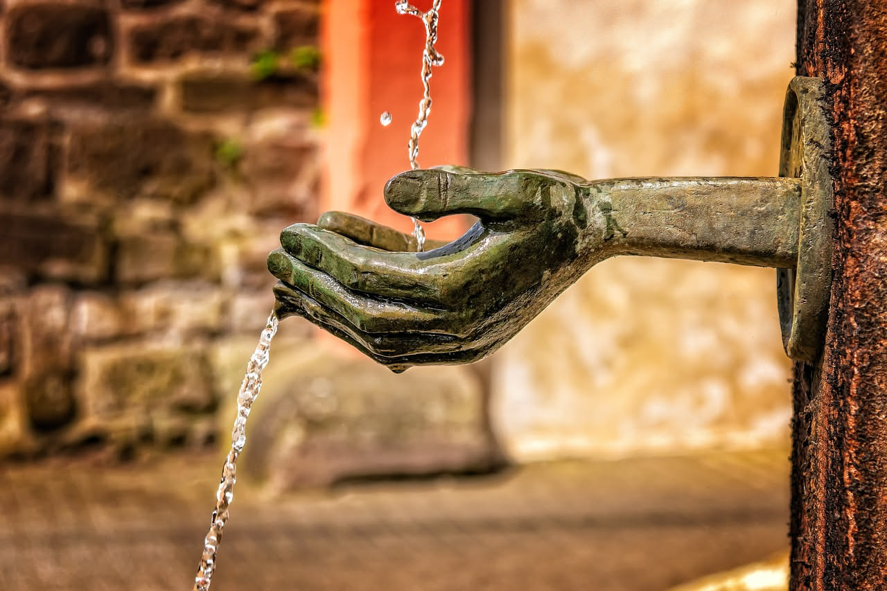 Mani di una persona immerse in una ciotola di acqua tiepida con vapore visibile, accanto a una lampada tenue su un comodino al tramonto