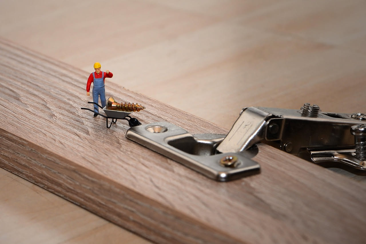 Cassetto di cucina in legno chiaro aperto parzialmente con guida metallica visibile sul lato interno, mano che esegue manutenzione