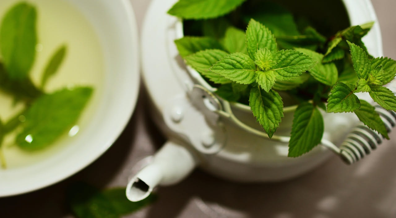 Persona che inala vapore da una ciotola di acqua calda con foglie di menta fresca, coperta con un asciugamano, in una stanza luminosa