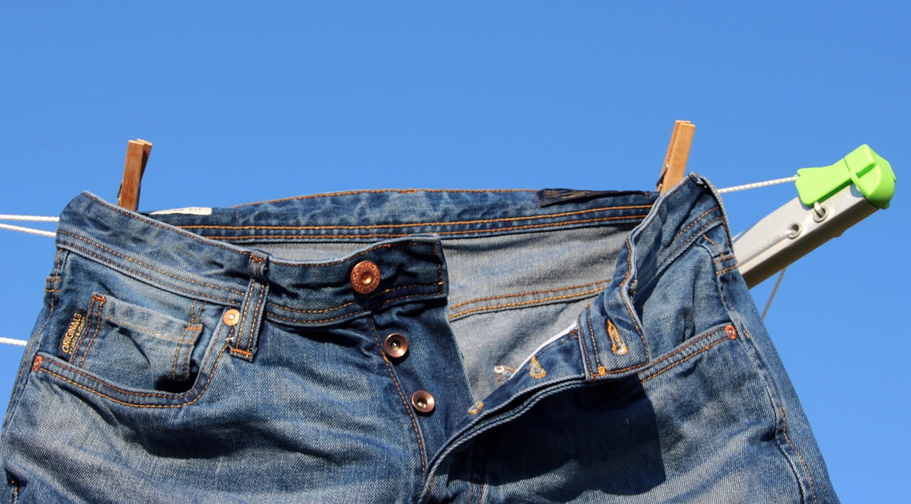 Dettaglio di macchia verde di erba su jeans azzurri con una mano che applica soluzione bianca con cotton fioc