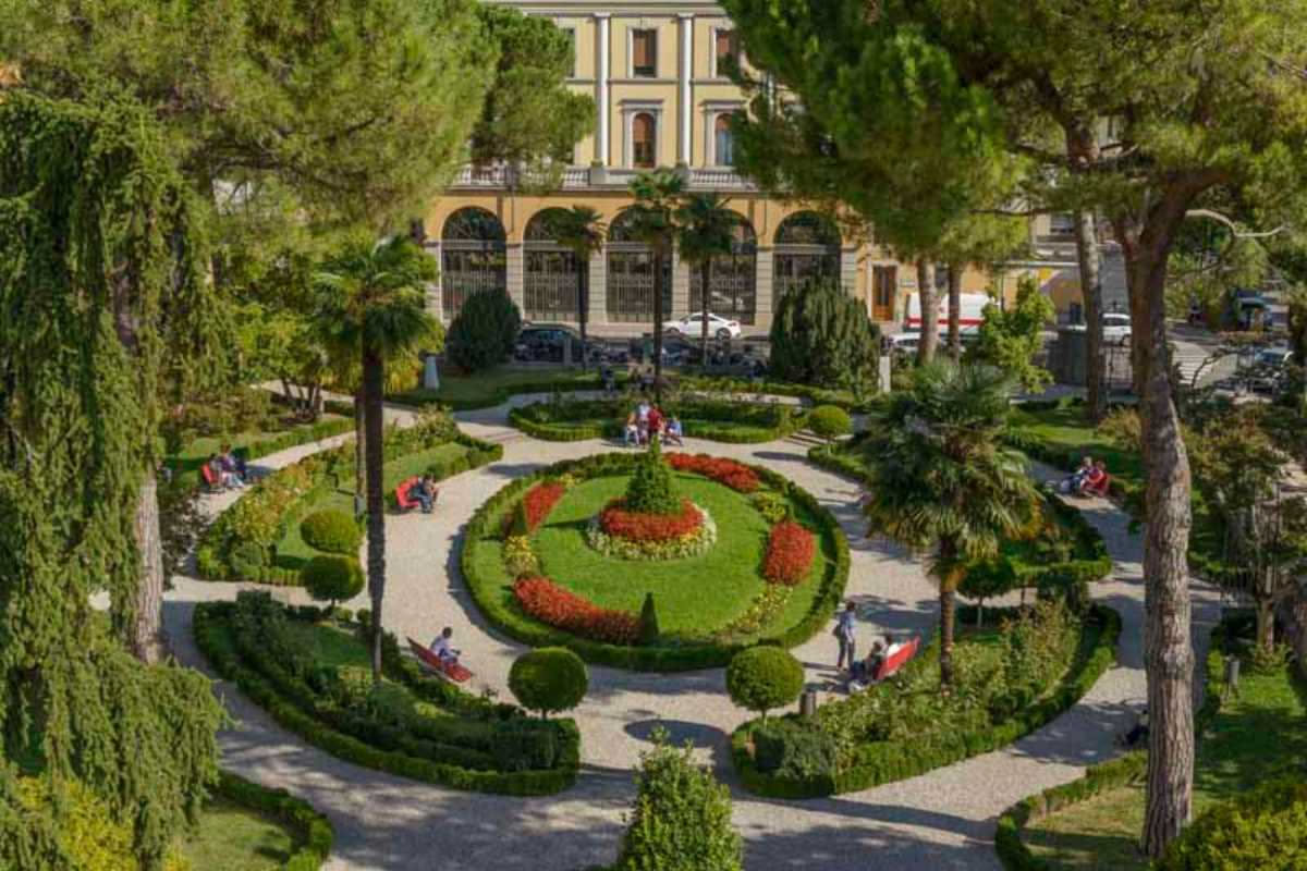 Giardino comune di un condominio con orto condiviso, panche in legno, una serra e diversi vicini che lavorano insieme tra le aiuole